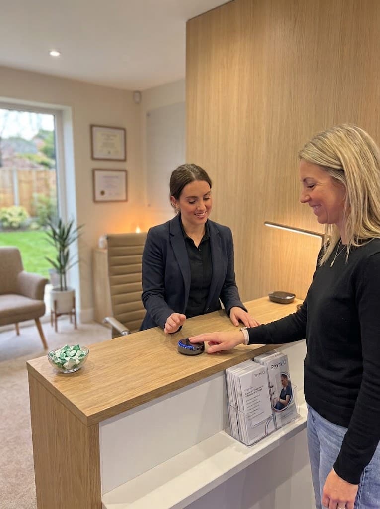 A client using the Prysm iO device at a practice reception desk while a receptionist assists